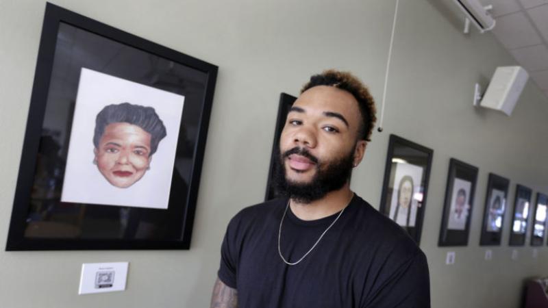 Jasaad Graves, wearing a black T-shirt, stands against a backdrop of portraits.