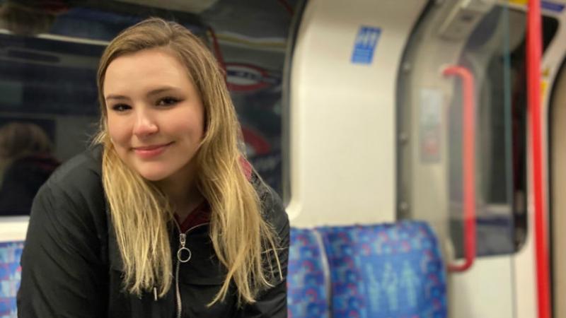 Caroline Garrow sits in a subway car wearing a black coat.