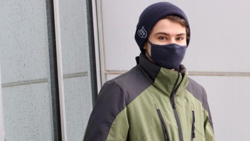Justin Williamson, wearing a navy blue mask and green jacket, looks at the camera.