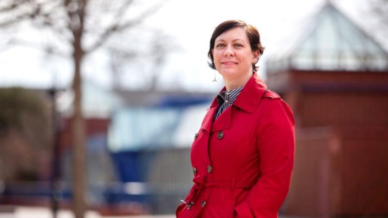 Beth Zinsli, wearing a long red jacket, stands in front of the Wriston Art Center.