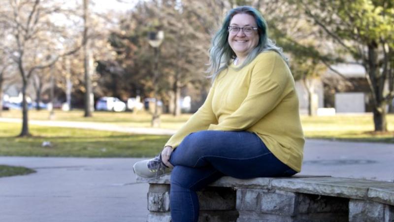 Deanna Donohoue sits on a stone bench and crosses her legs.