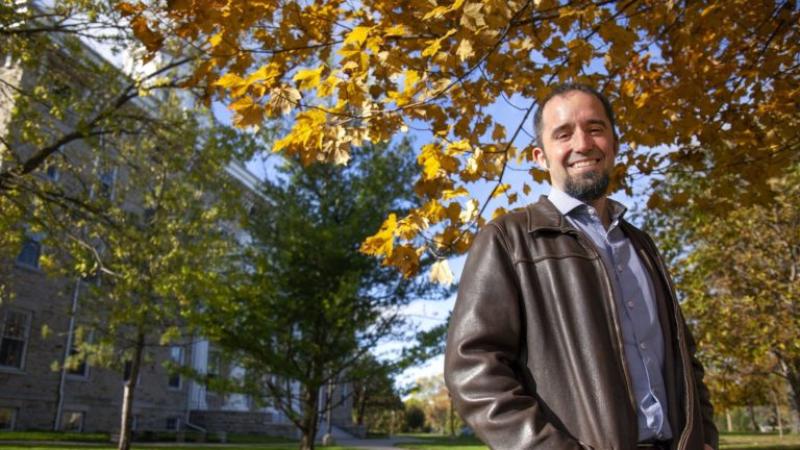 Stefan Debbert smiles at the camera, standing against a backdrop of deciduous trees.