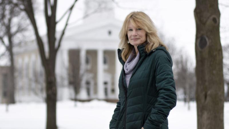Patty Darling stands, wearing a black winter coat, against a backdrop of a snow-covered Main Hall Green.