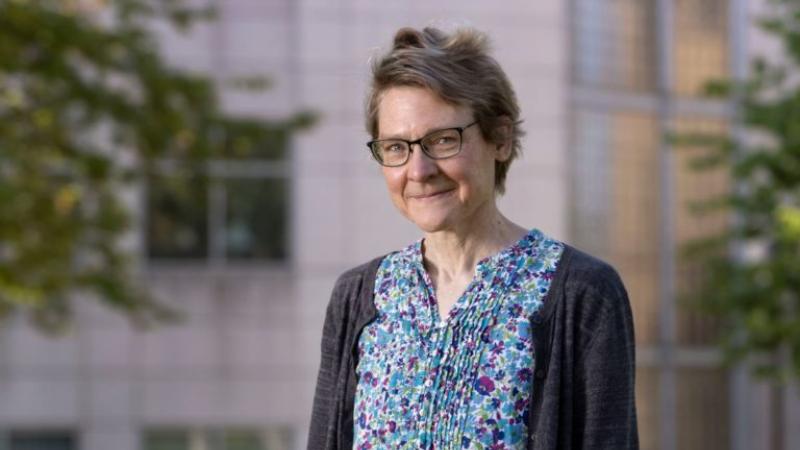 Marcia Bjornerud, wearing a blue floral shirt and a grey cardigan, smiles at the camera.