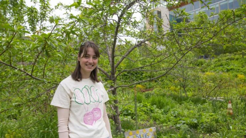 Phoebe Eisenbeis stands amid greenery with a small "SLUG Garden" sign on the ground.