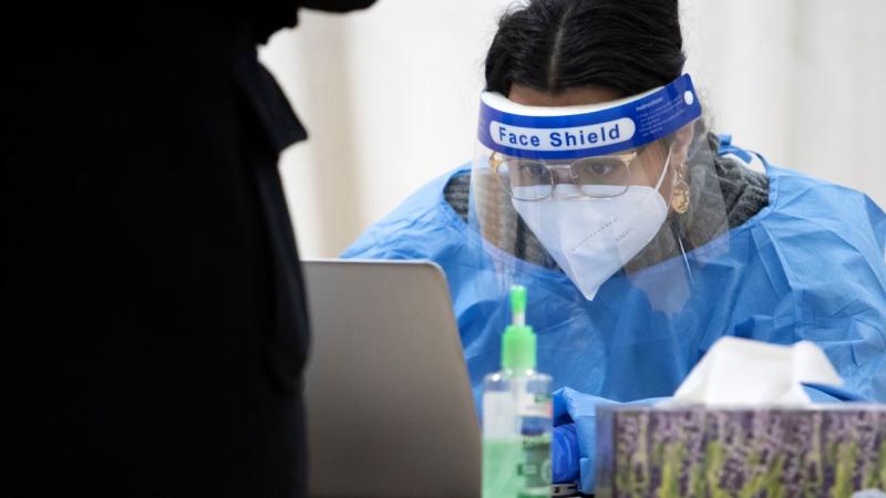 student worker, using protective gear, signs people up in the computer for their COVID-19 test