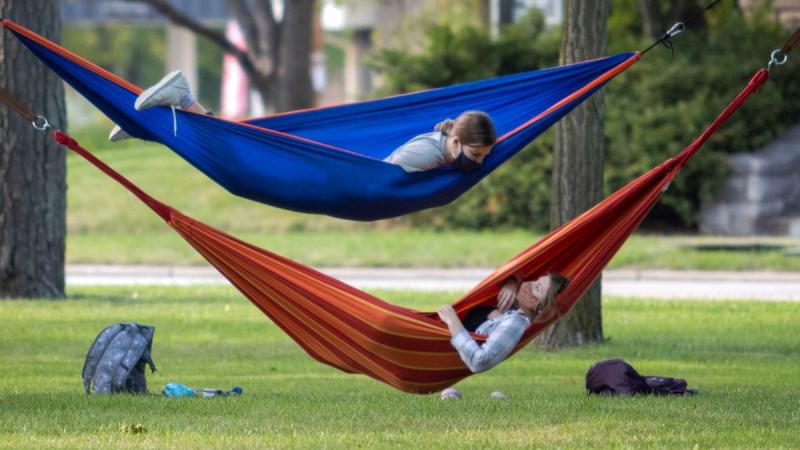 Two students talking while they hang in their own outdoor hammocks. 