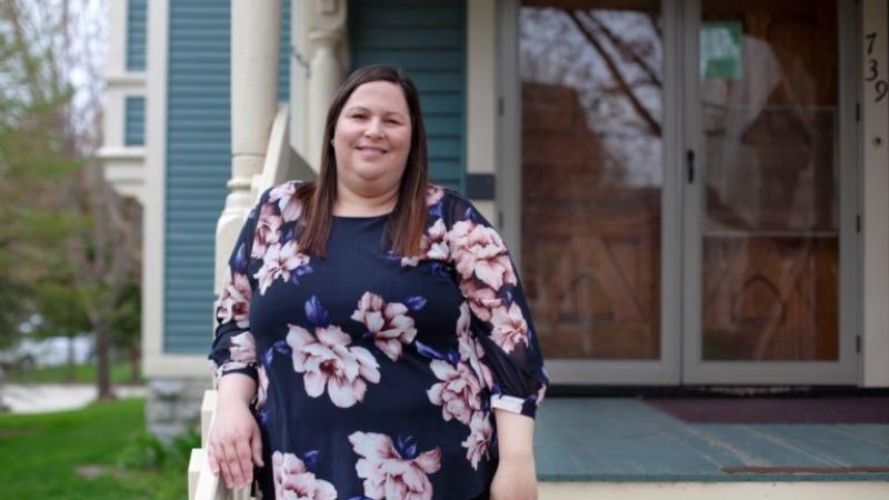 Lezlie Weber, wearing a floral shirt and leaning on a railing, smiles at the camera.