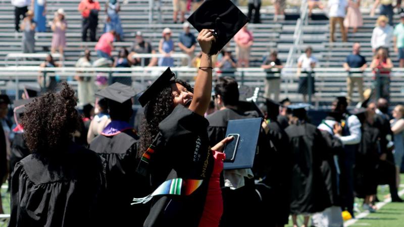 Graduates and a student showing their diploma during commencement 