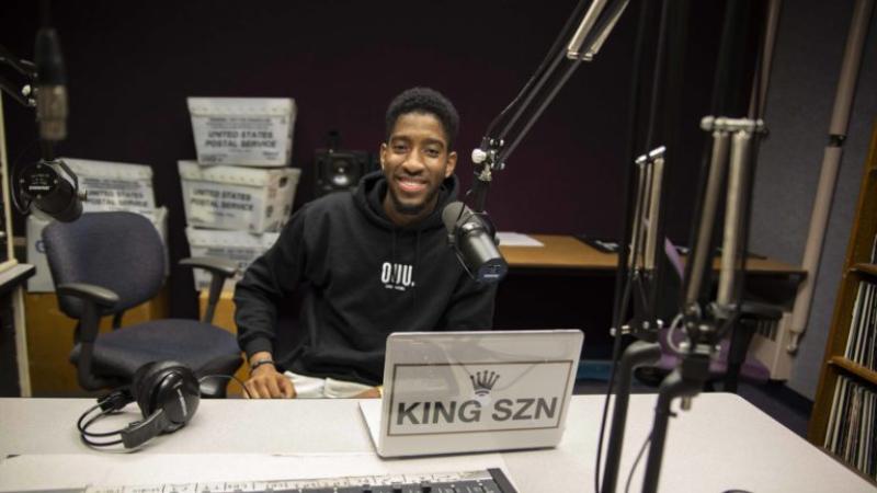 De Andre King, surrounded by DJ equipment, smiles at the camera.