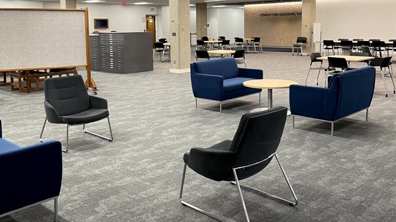 Large, open space with padded chairs, small tables, and the center for academic success in the background.
