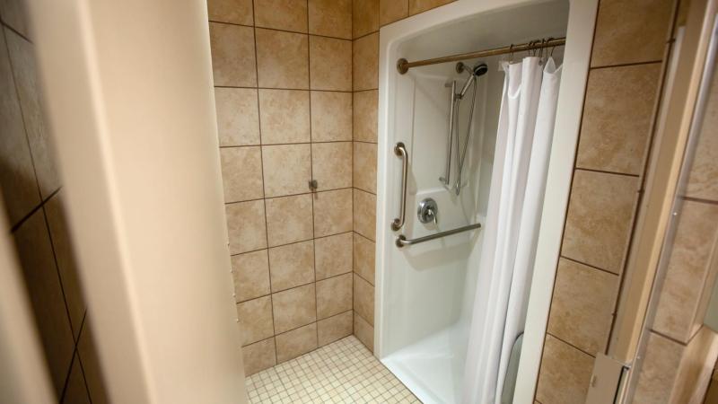 single stall shower with handles and white curtains in brown tiled bathroom