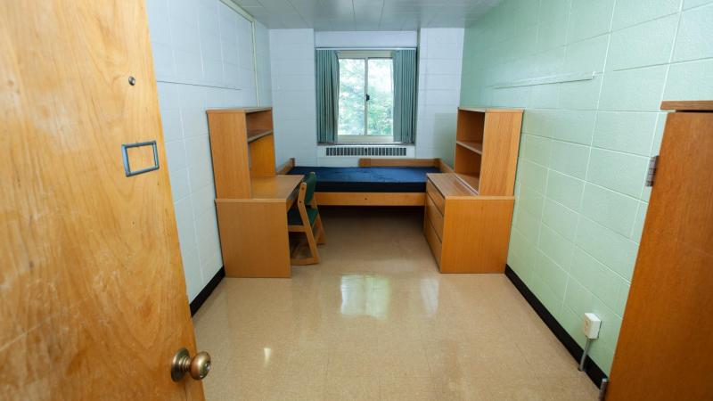 room with wooden desk and dresser, and XL twin bed under small window