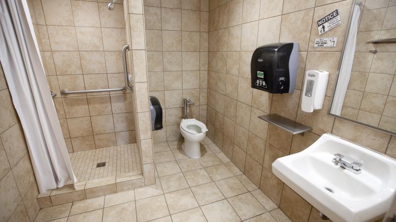 beige tiled bathroom with shower with white curtain, toilet, sink and paper towel dispenser 