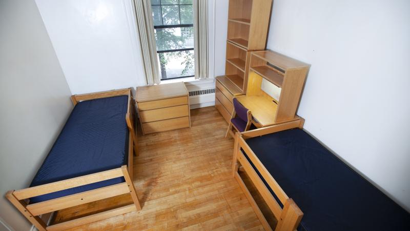 room with small window, two XL twin beds, two wooden dressers, bookshelves, and desks