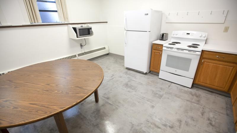 large kitchen with fridge, electric-range stove, microwave and a large round table 