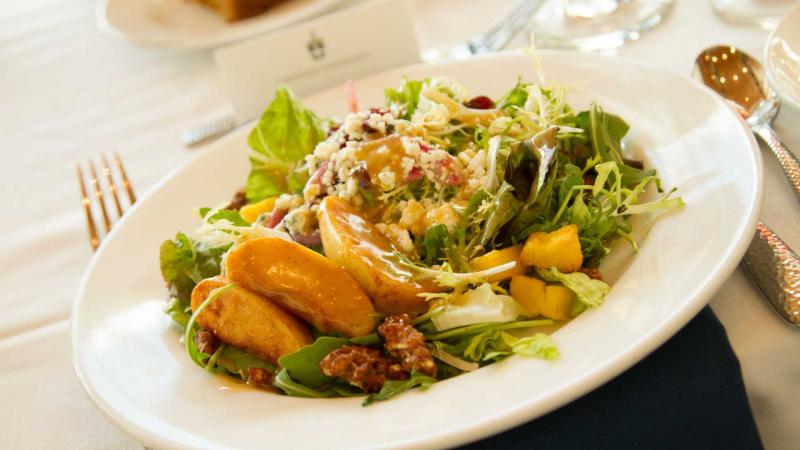 Salad with chicken and peaches on white dinner plate with silver utensils