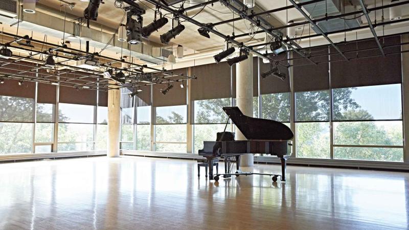 Grand piano in open space with ceiling-to-floor windows and performance lighting. 
