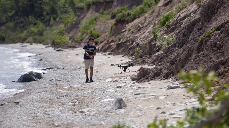 Student walking along the shore of Lake Michigan while using a drone 