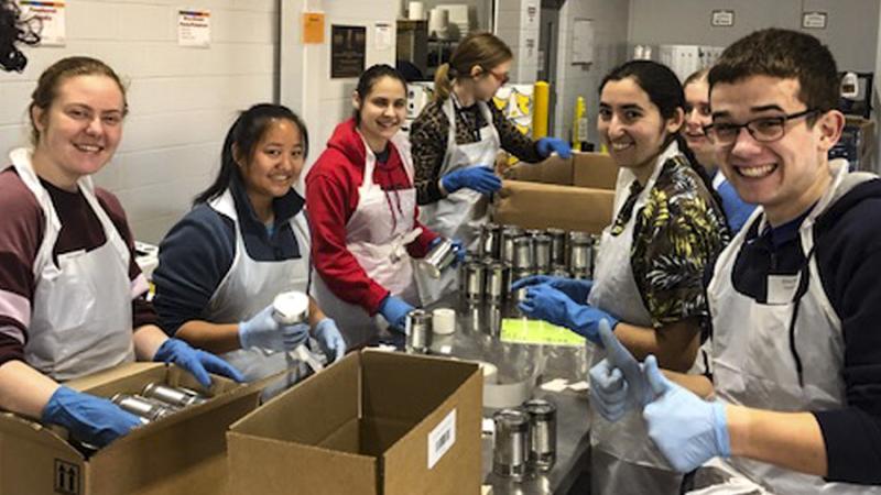 Students using gloves and aprons smiling at the camera while volunteering  