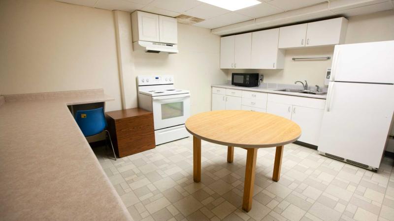 Large kitchen with long counter along a wall, full-range stove, white cabinets, microwave, sink and fridge; a round wooden dining table stands in the middle of the room