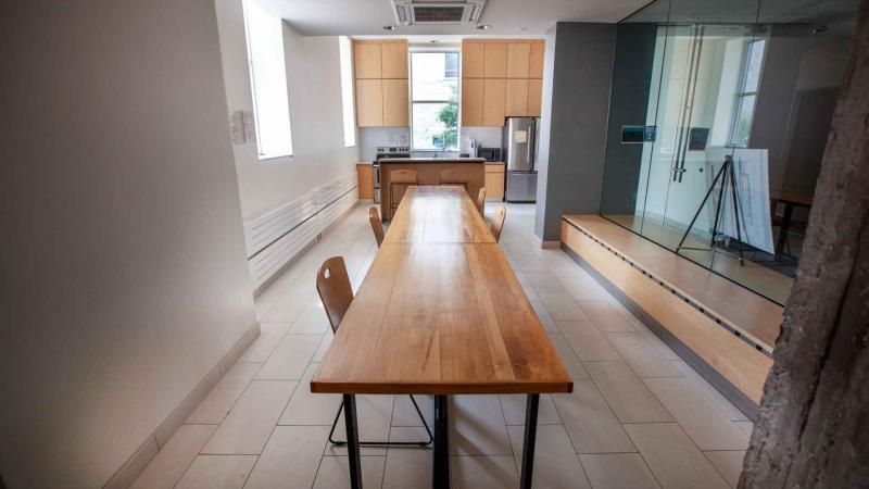 Long modern dining table with sink, wood cabinets and stainless steel fridge at the end