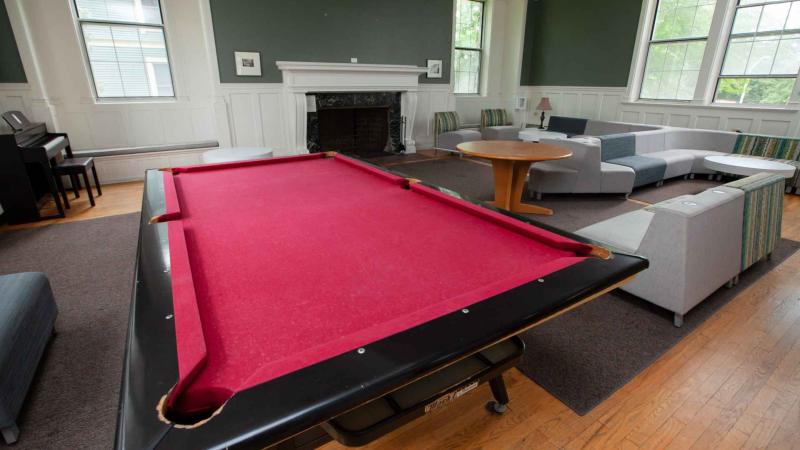Pool table in middle of formal lounge with a fireplace in the background and table and section sofas to the table's right