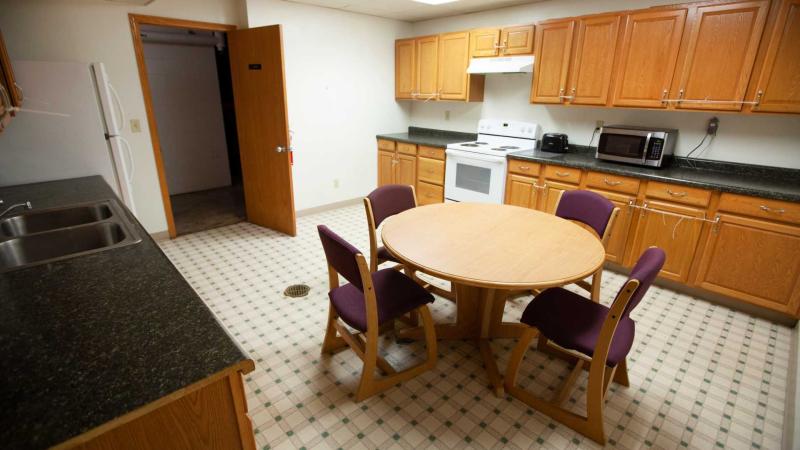 Large kitchen and dining room with full-rage stove, microwave, sink and cabinets along a wall; and a round table with chairs around it in the middle of the room