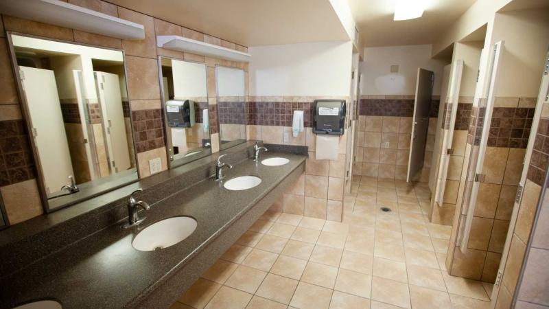 Large tiled bathroom with multiple stalls and sinks with mirrors over each