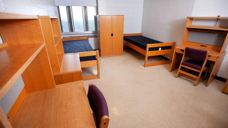 Dorm room with two XL twin beds, wooden desks, shelves and drawers with one window