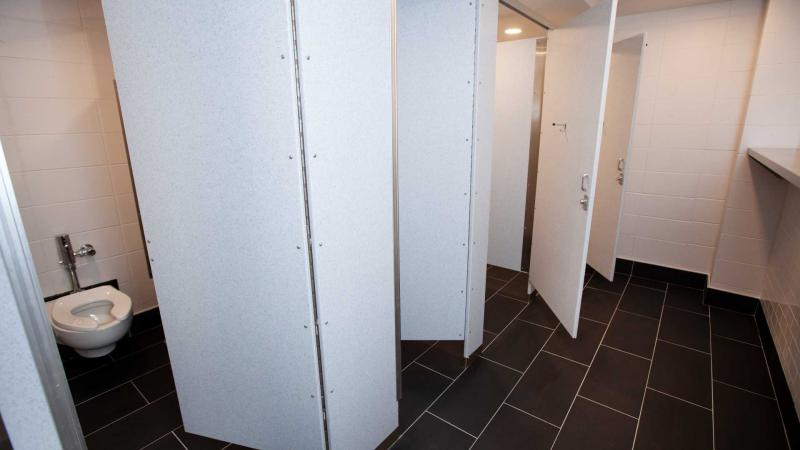 Four bathroom stalls in a shared bathroom with black tiled floors