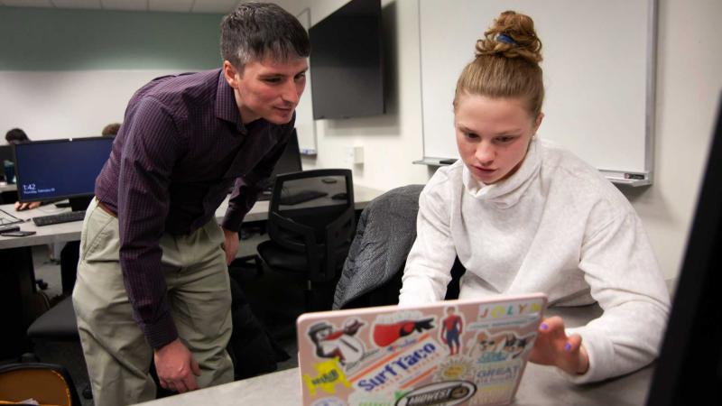 computer science professor helping student on laptop during class