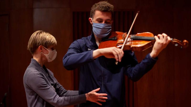 theater professor adjusting violin student's stance as they play