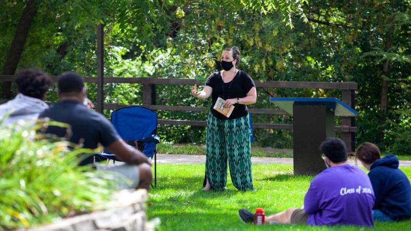 Professor lecturing to group of students sitting on the lawn