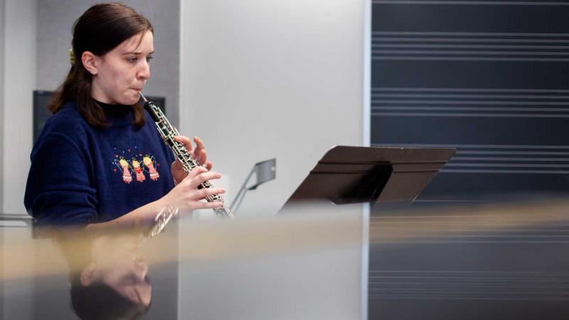 Marlee Matthews, a junior, performs in oboe studio with her reflection on a piano in the foreground.