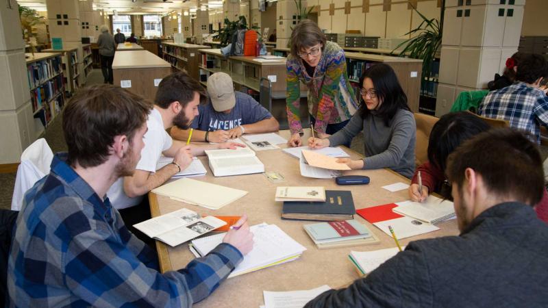 history professor helps students seated around table in library 