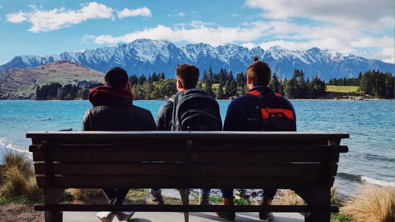 Students resting on bench by mountains and lake