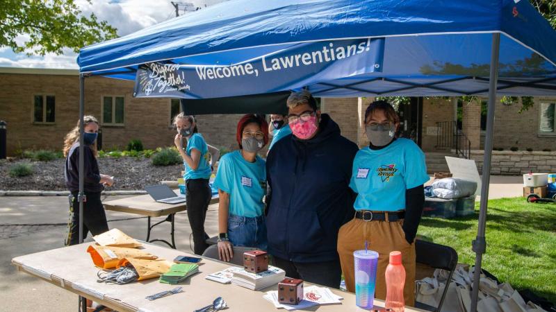 Group of community advisors stand under tent at check-in table during new student move-in