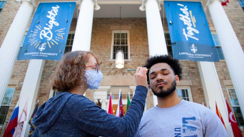 Claire Chamberlin, a junior, paints the face of Jose Otero. A first-year, during the Blue and White Weekend Block Party on Main Hall Green.