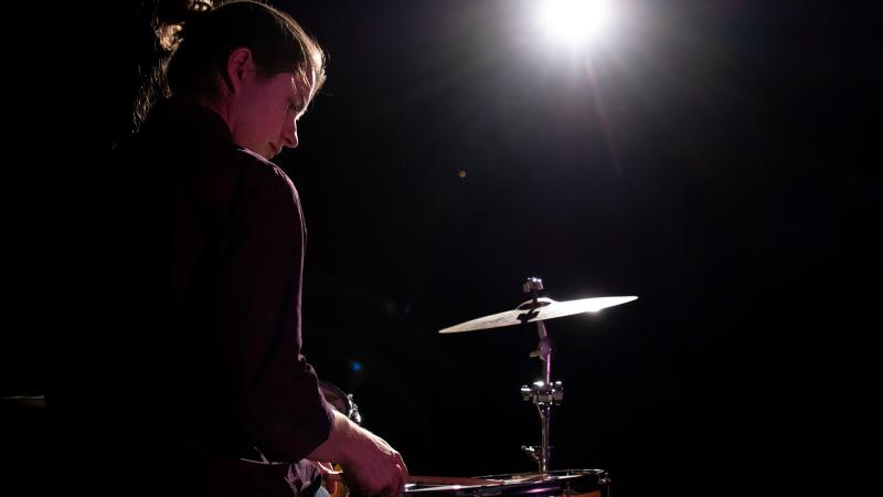 Drummer performing on stage with a spotlight shining 