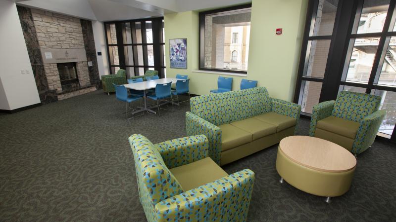 Hiett Hall lounge with fireplace and various types of seating with large, floor-length windows.