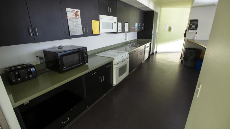 Hiett Hall kitchen with long countertop and row of cabinet with a microwave, stove and oven and sink.