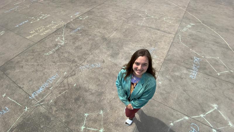 Avery Greene stands on a sidewalk decorated with chalk drawings of constellations.