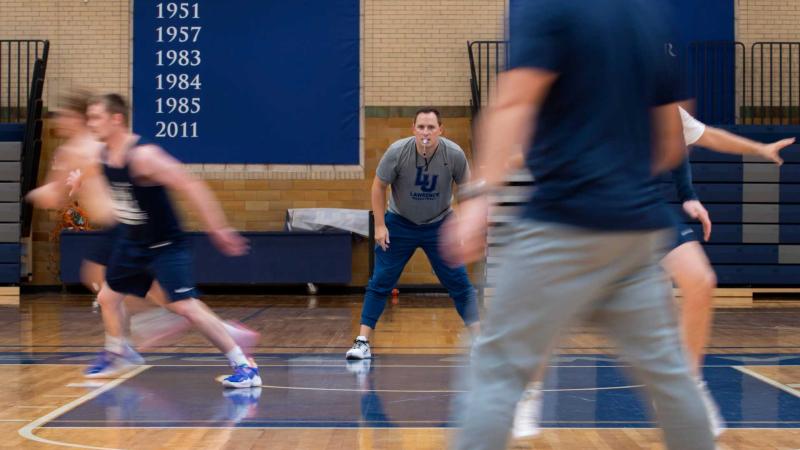 Lawrence's new men's basketball coach stands on sidelines while players jog across the court.