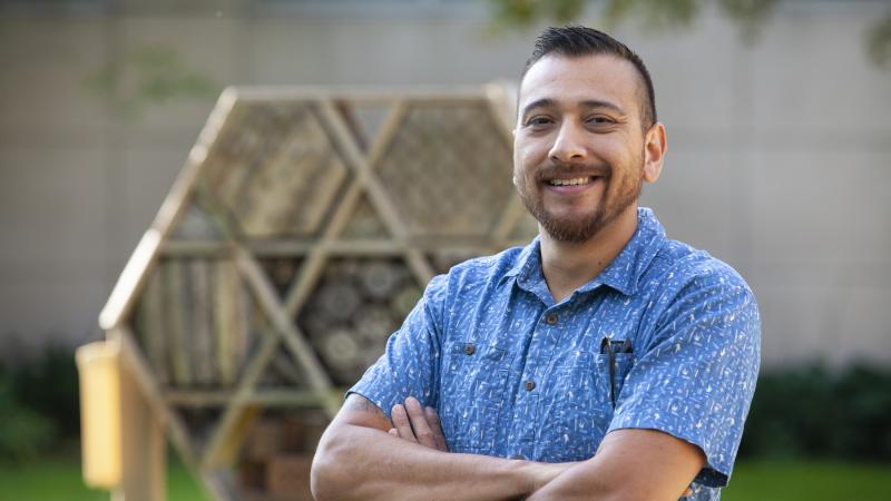 Israel Del Toro, wearing a blue shirt, stands in front of a bee-friendly structure.