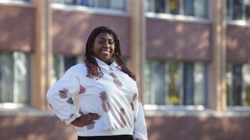 Ladora Thomas poses in front of a brick building, wearing a shirt with a pineapple pattern.