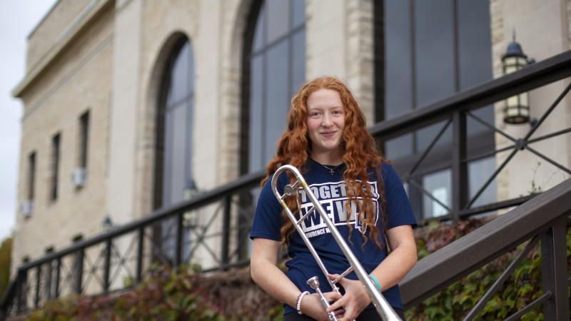 Mallory Meyer, wearing a Lawrence T-shirt, holds her trombone.