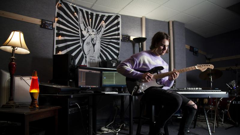 Michael Murphy, surrounded by instruments and recording equipment, plays the electric guitar.