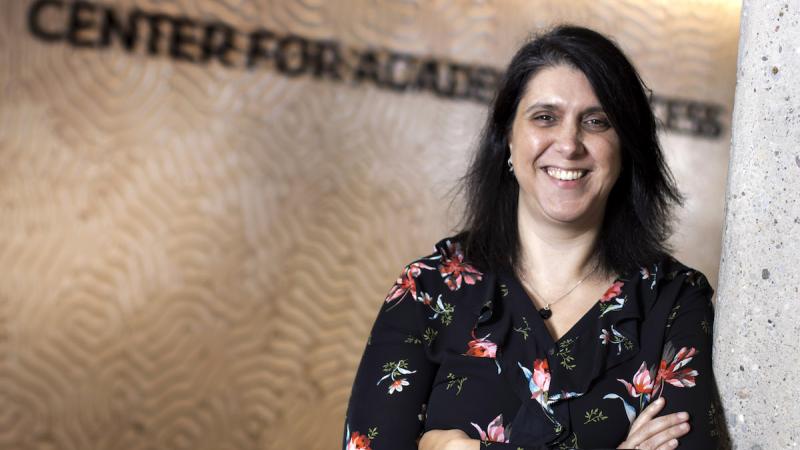 Monita Mohammadian Gray, wearing a floral patterned shirt, poses against a wall in the Center for Academic Success.