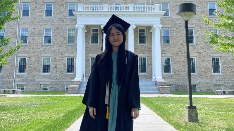 Doan Thu Thuy Nguyen in cap and gown in front of Main Hall.